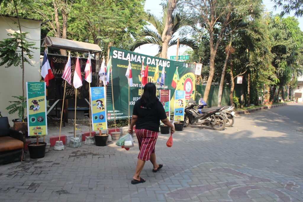 Warga melewati depan bendera dan hiasan banner menyambut Piala Dunia U-17 di Manukan Lor IV-K, Surabaya, Selasa (31/10/2023). Foto: Athalia magang suarasurabaya.net