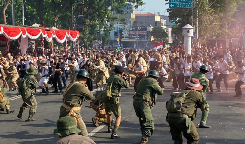 Atraksi pertempuran 10 November 1945 yang berlangsung di Jalan Pahlawan Kota Surabaya. Nampak puluhan orang memeragakan pertempuran setelah suara dentuman terdengar nyaring menandai dimulainya perang, Minggu (5/11/2023). Foto: Wildan suarasurabaya.net