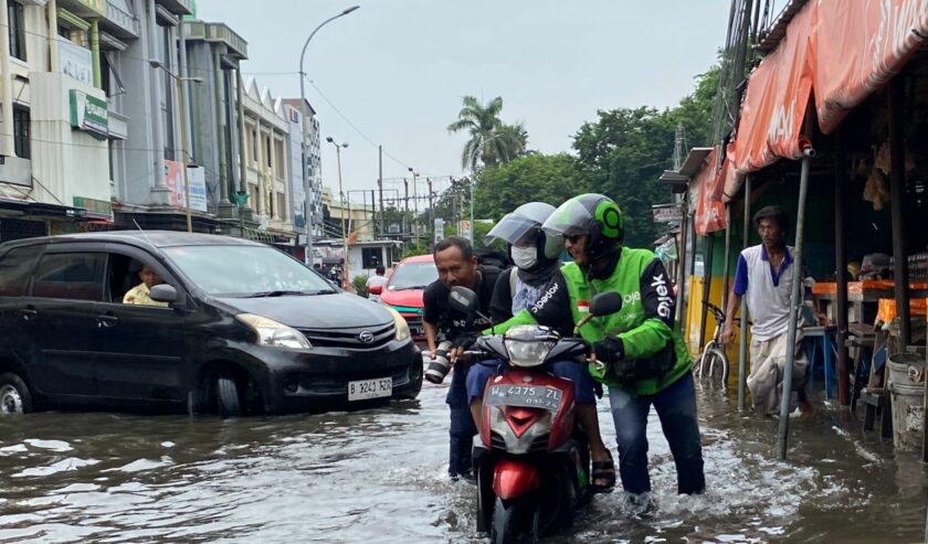 Seorang driver ojol harus menerobos genangan air di Jalan Raya Pepelegi sambil tetap mengangkut penumpangnya, Rabu (7/2/2024). Foto: Wildan suarasurabaya.net