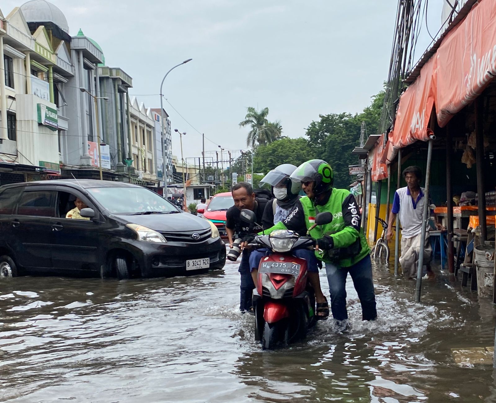Seorang driver ojol harus menerobos genangan air di Jalan Raya Pepelegi sambil tetap mengangkut penumpangnya, Rabu (7/2/2024). Foto: Wildan suarasurabaya.net