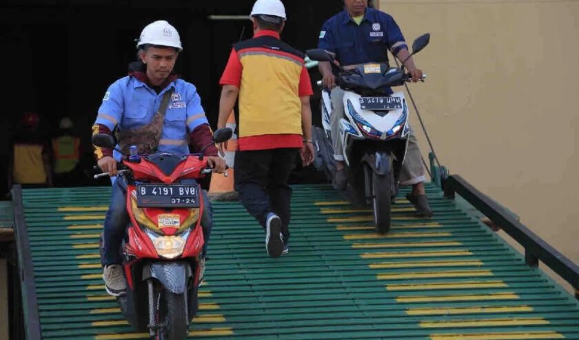 Ilustrasi - Seseorang melintas di antara dua orang yang sedang mengeluarkan dua motor dari kapal laut. Foto: Antara