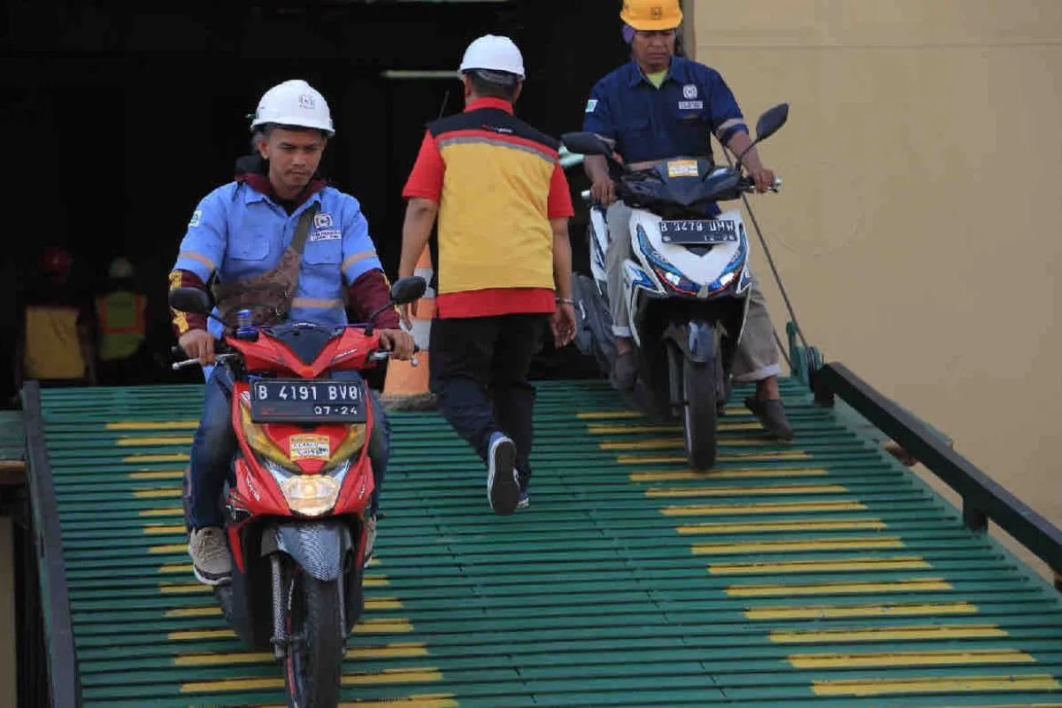 Ilustrasi - Seseorang melintas di antara dua orang yang sedang mengeluarkan dua motor dari kapal laut. Foto: Antara