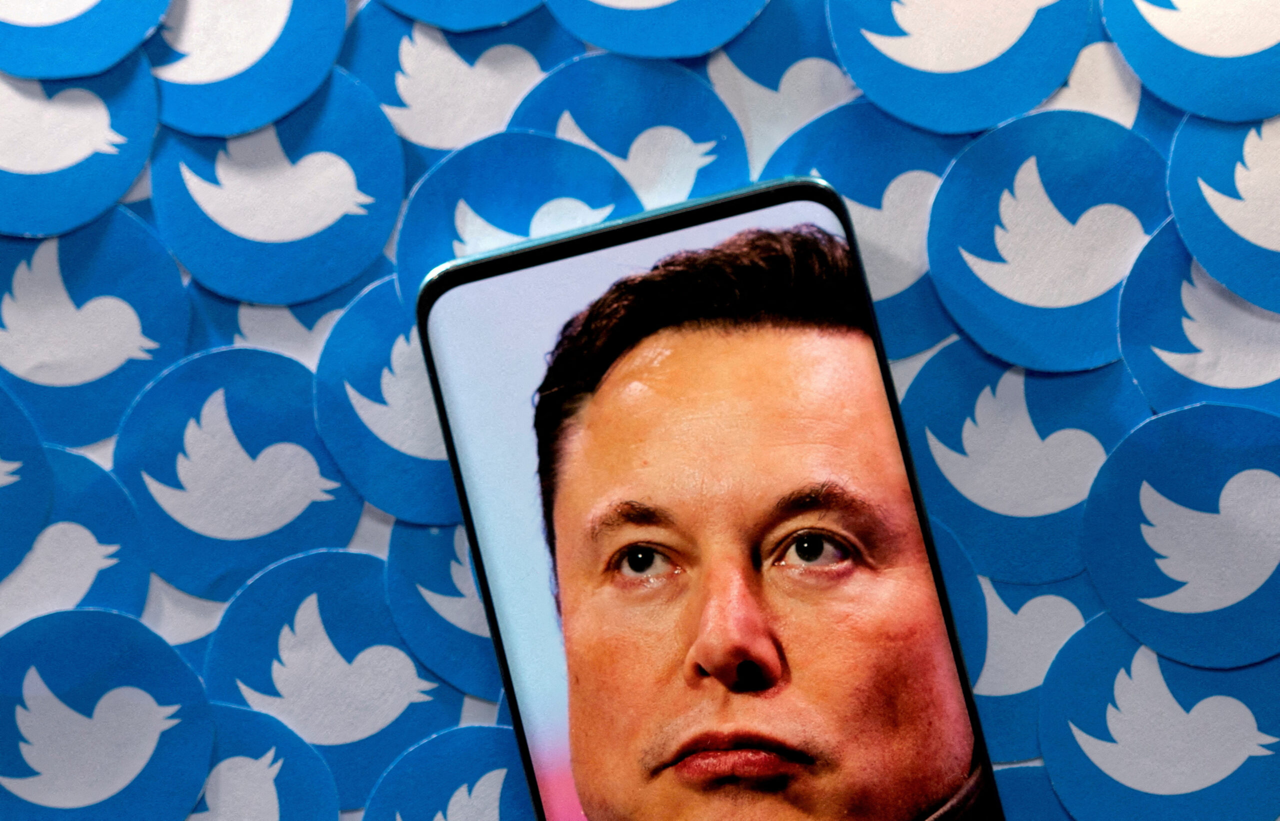 Ilustrasi gambar Elon Musk terlihat di smartphone yang ditempatkan pada cetakan logo Twitter. Foto: Reuters