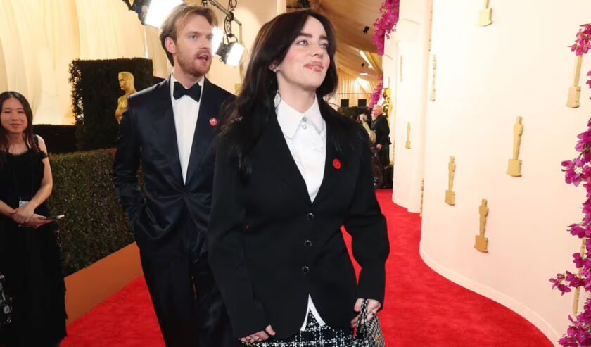 Musisi wanita Billie Eilish tampak mengenakan pin merah dengan lambang telapak tangan mengelilingi hati hitam, pada busana yang dikenakan di karpet merah perhelatan Oscar 2024, Minggu (10/3/2024) petang waktu Los Angeles, Amerika Serikat, atau Senin (11/3/2024) sekitar pukul 04.44 WIB. Foto: Reuters