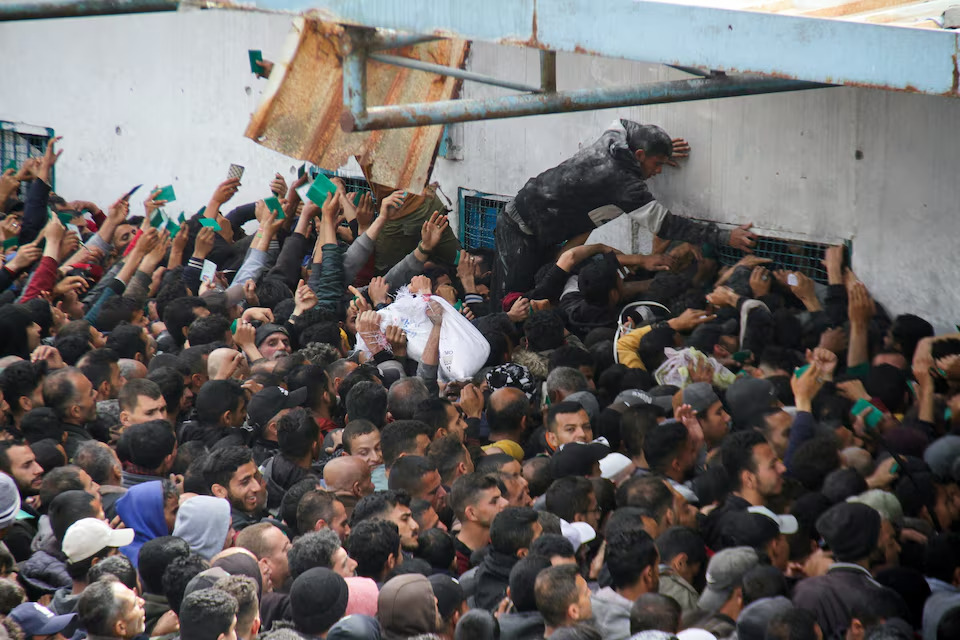 Warga Palestina berkumpul untuk menerima bantuan di luar gudang UNRWA ketika penduduk Gaza menghadapi krisis kelaparan, di Kota Gaza, Senin (18/3/2024). Foto: Reuters