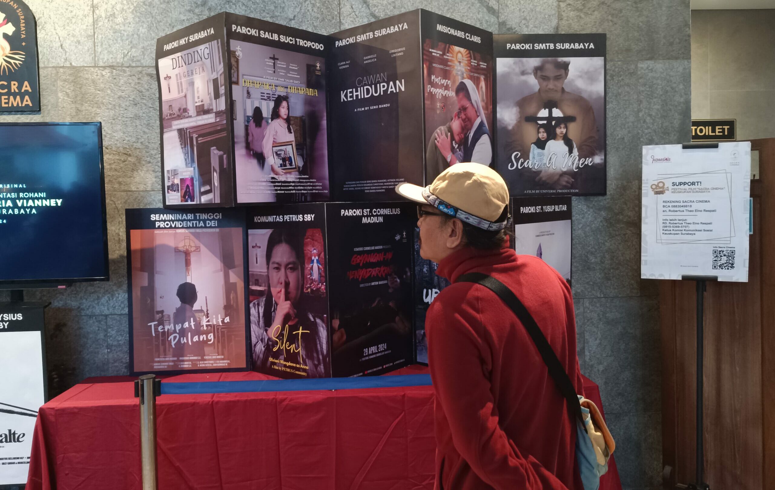Salah satu pengunjung saat melihat beberapa pameran poster hasil Festival Film Sacra Cinema di Galera Sacra Cinema Gereja Katolik Hati Kudus Yesus (HKY) Katedral Surabaya, Sabtu (11/5/2024). Foto: Risky suarasurabaya.net