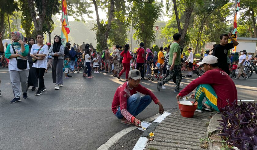 Petugas kebersihan Taman Bungkul yang ikut mengecat trotoar jalur tengah di, Minggu (12/5/2024). Foto: Firman magang suarasurabaya.net